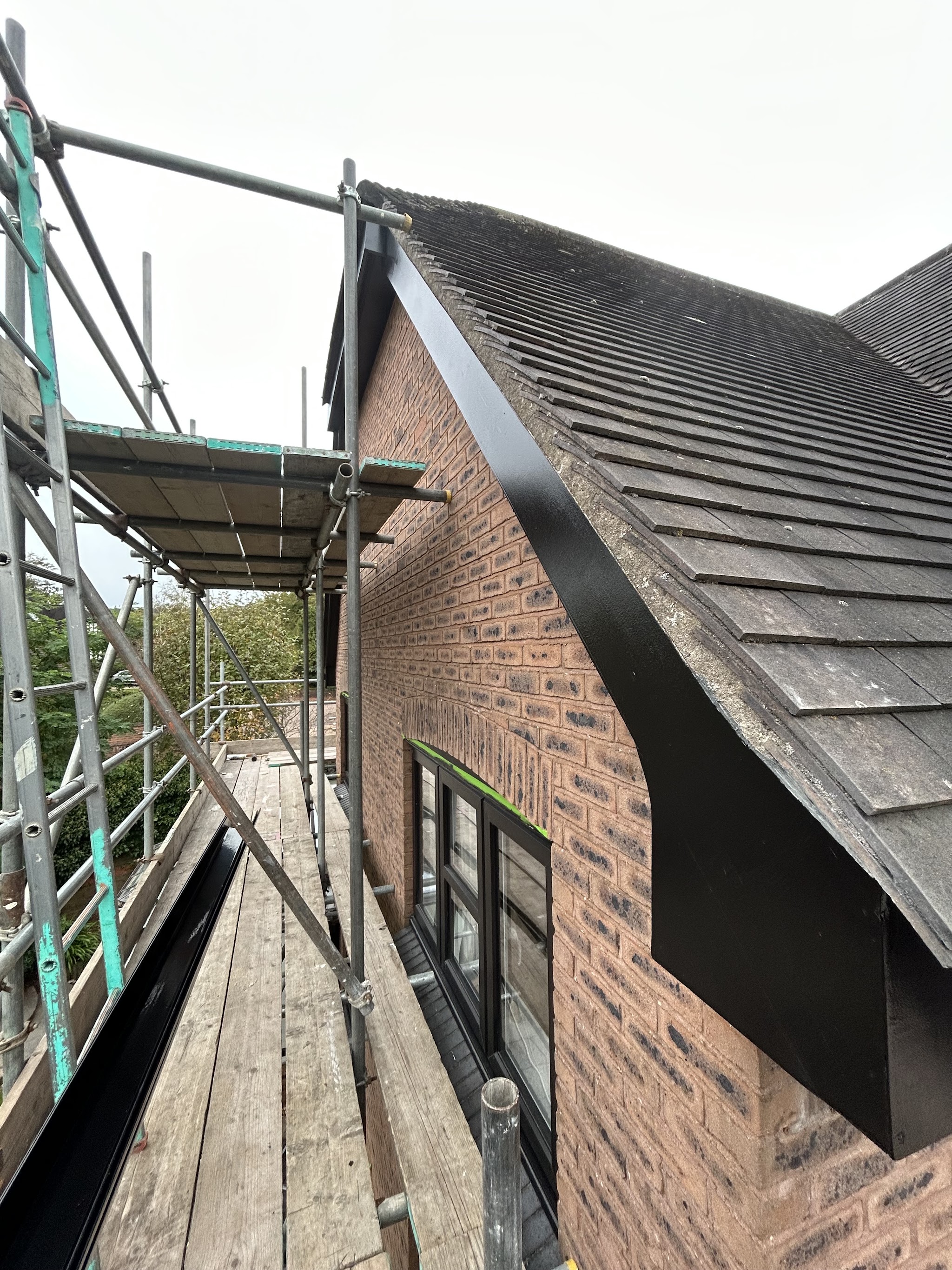 Exterior work from the scaffold on a brick gable with fresh black fascia and bargeboards