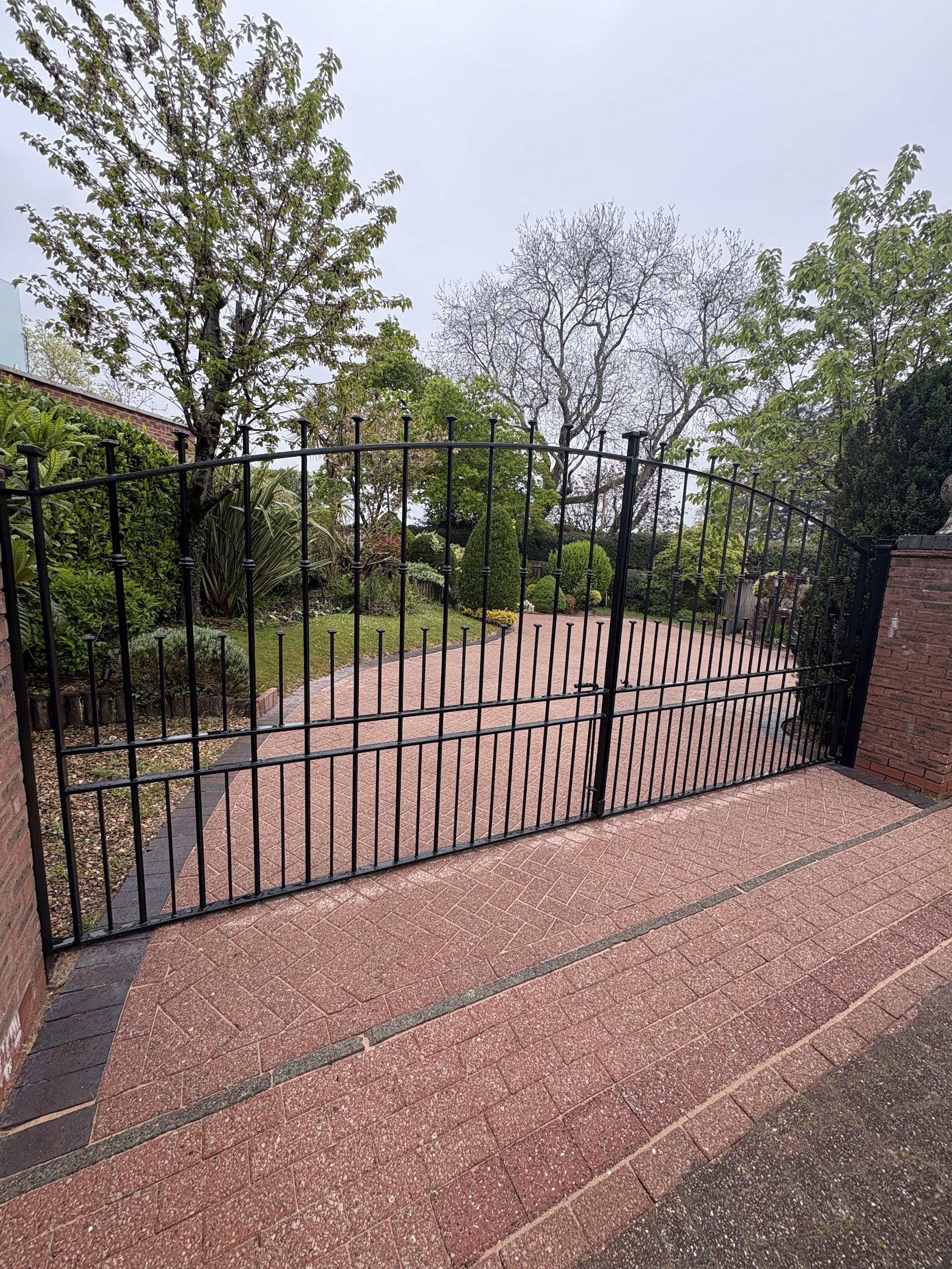 Black painted metal driveway gates and railings beside a block paved drive